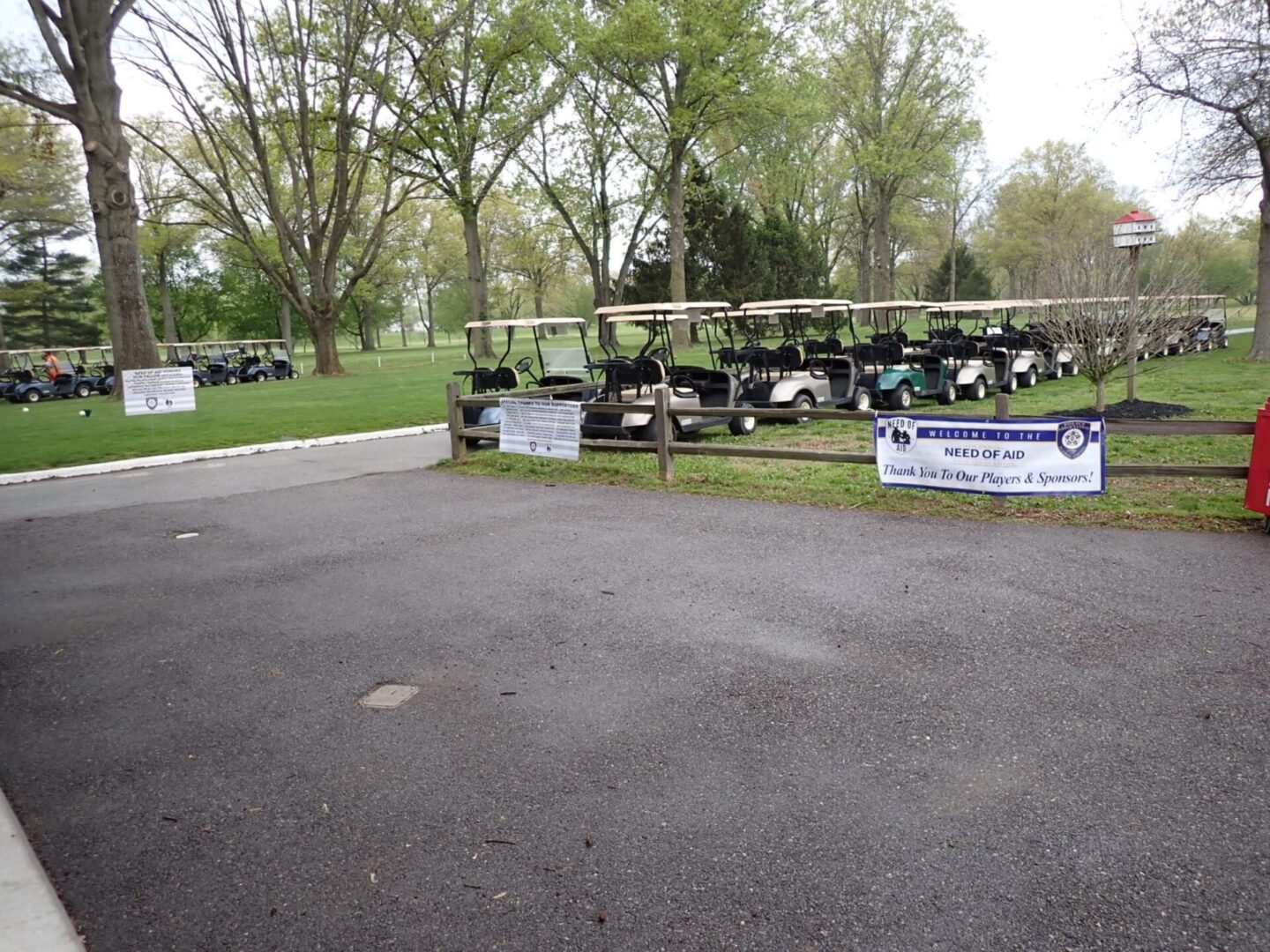 Golf carts parked in a row beside banners at an outdoor event.