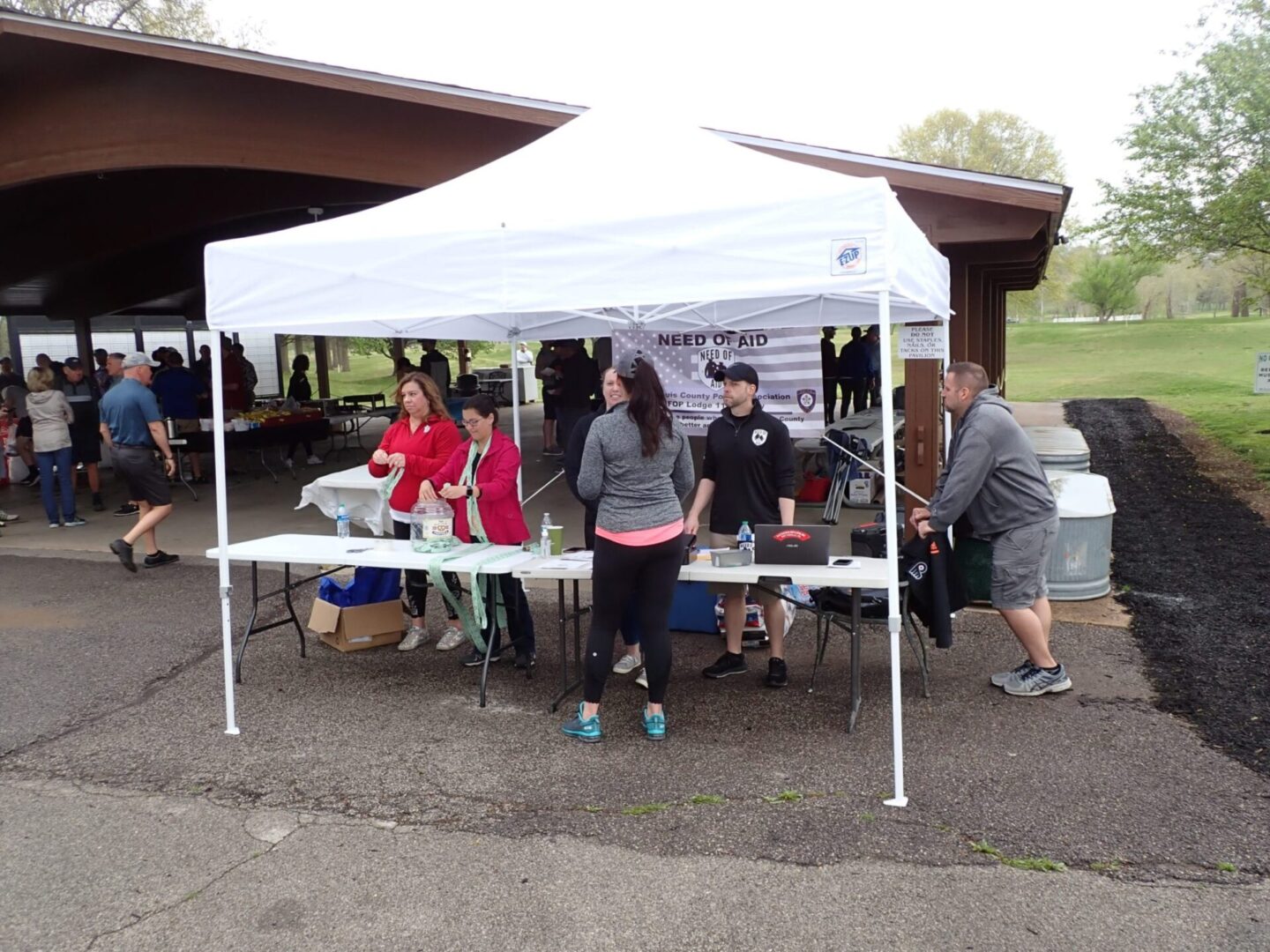 A group of people gathered under a white canopy tent at an outdoor event.