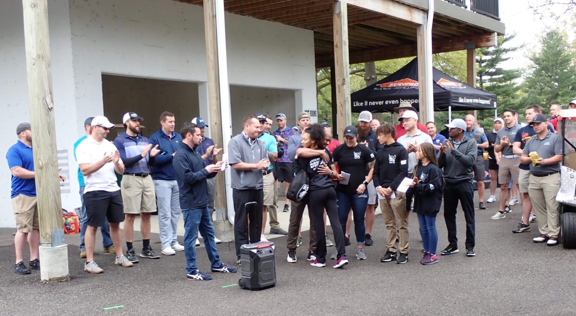 Group of people gathered outdoors, some clapping and holding drinks.