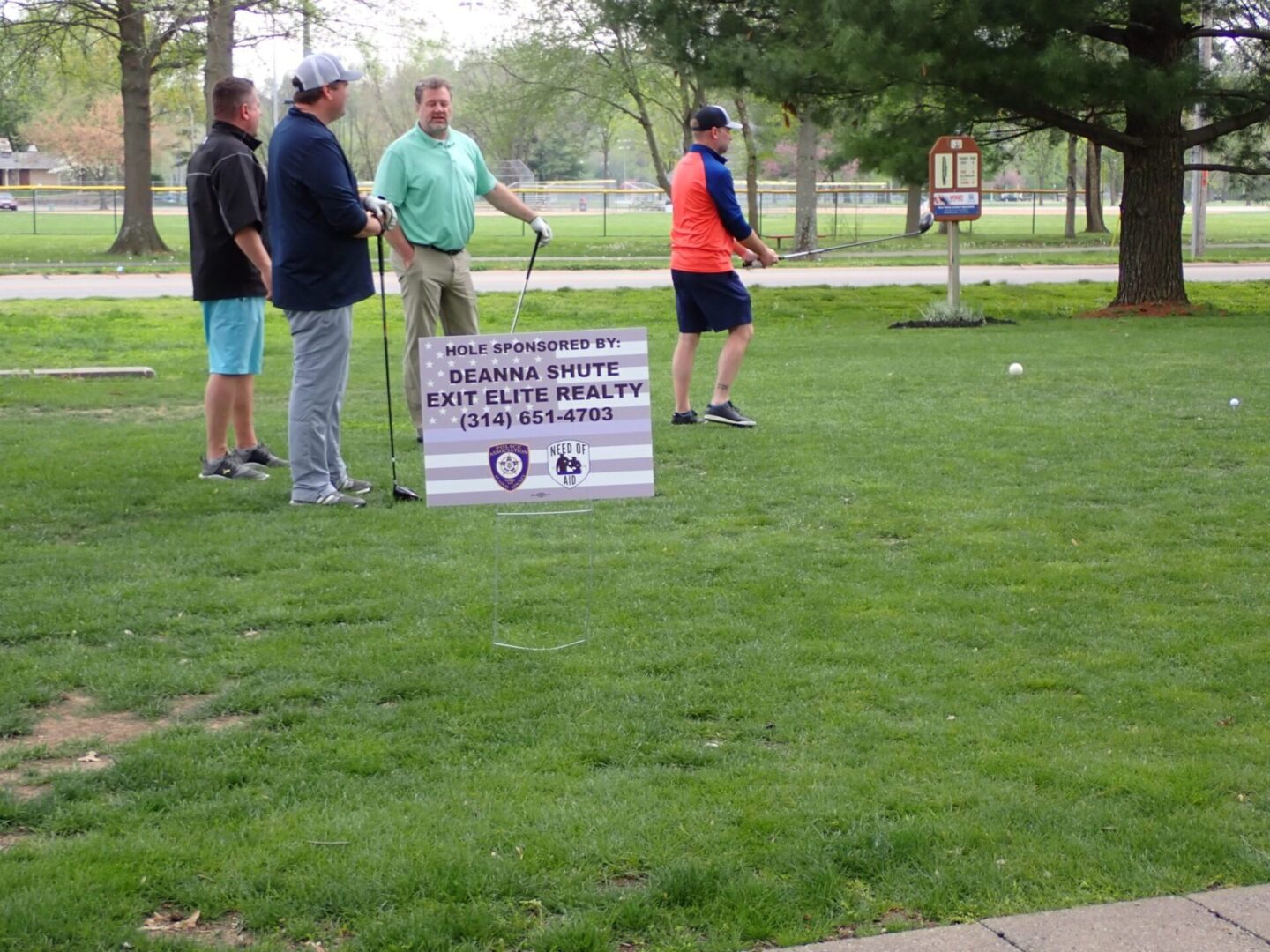 Group playing croquet in a park with a sign about social distancing.