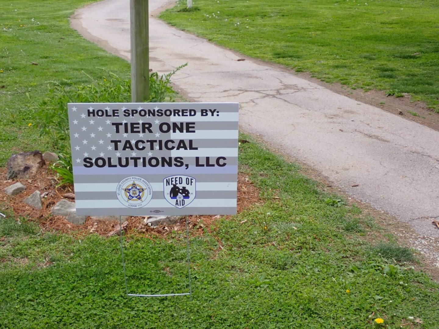 Sign for a hole sponsored by Tier One Tactical Solutions, LLC on a golf course.