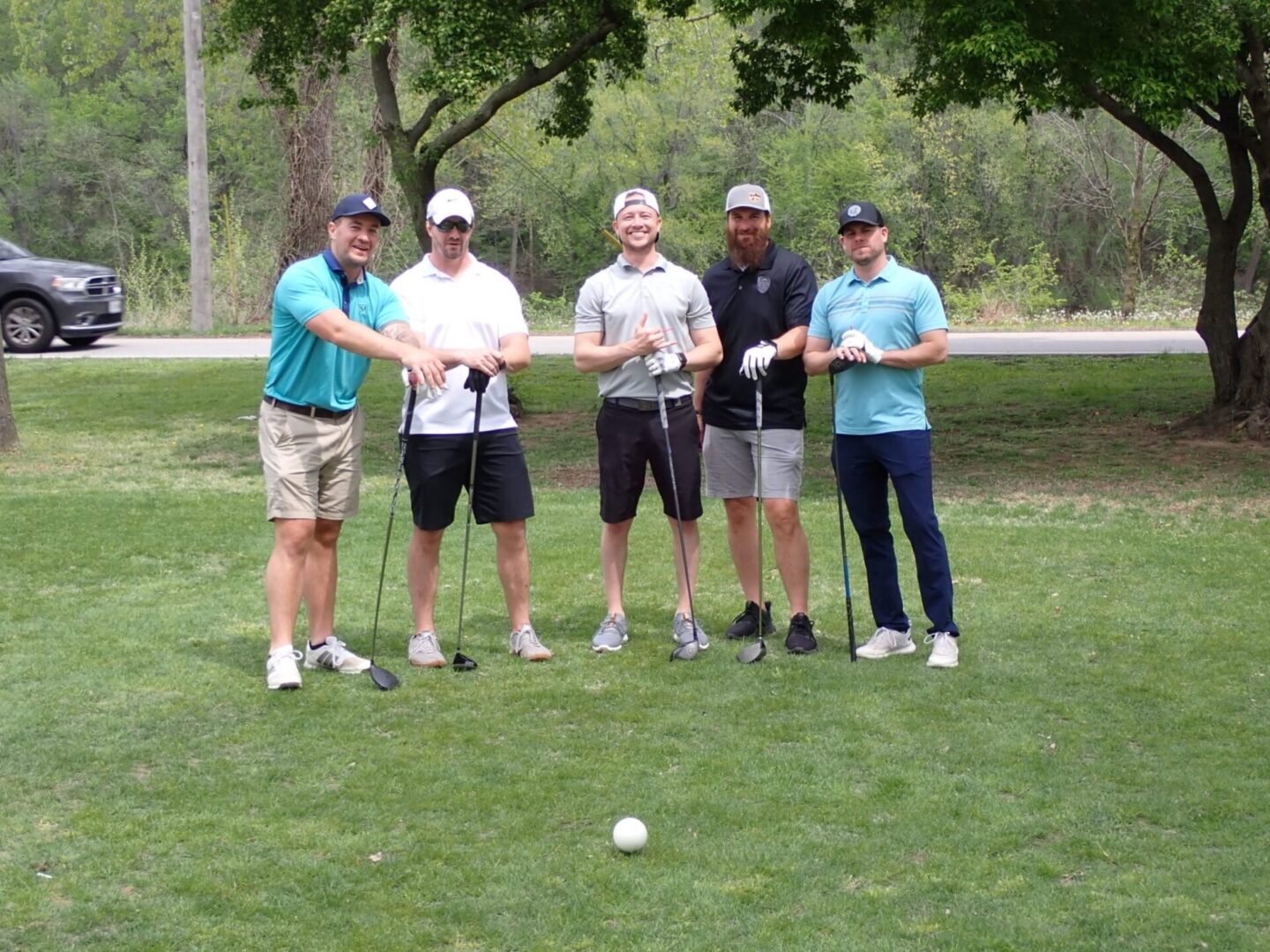 Five men standing on a golf course with golf clubs.