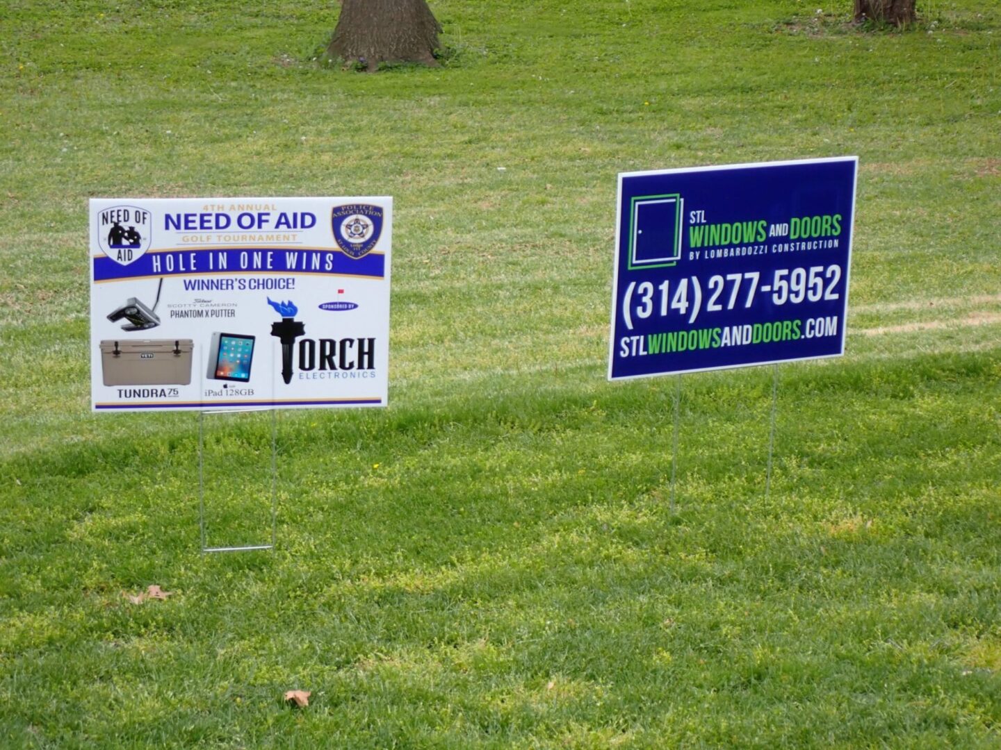Two yard signs on a grassy area seeking aid and phone assistance.