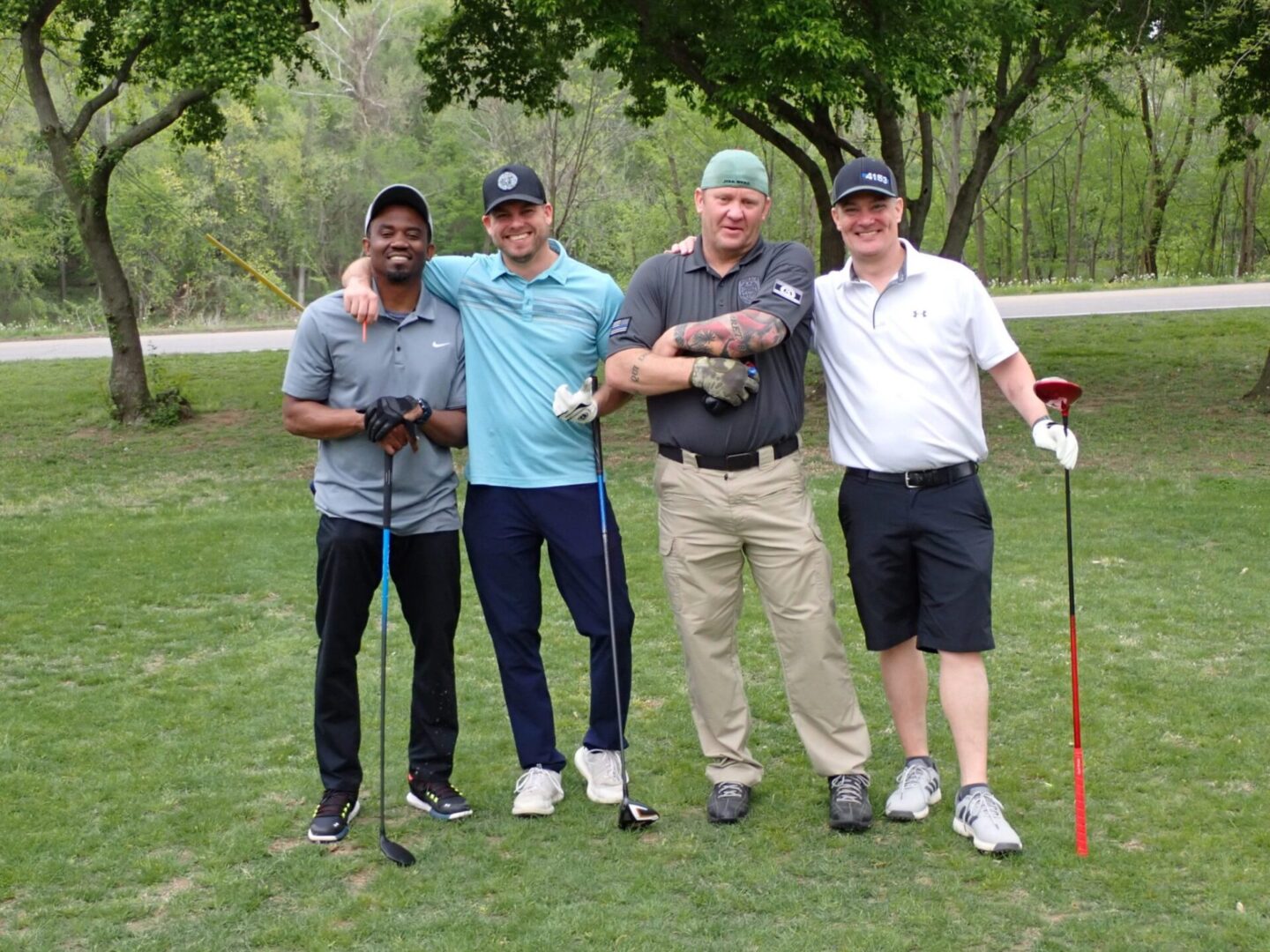 Four men posing outdoors with golf clubs on a green lawn.
