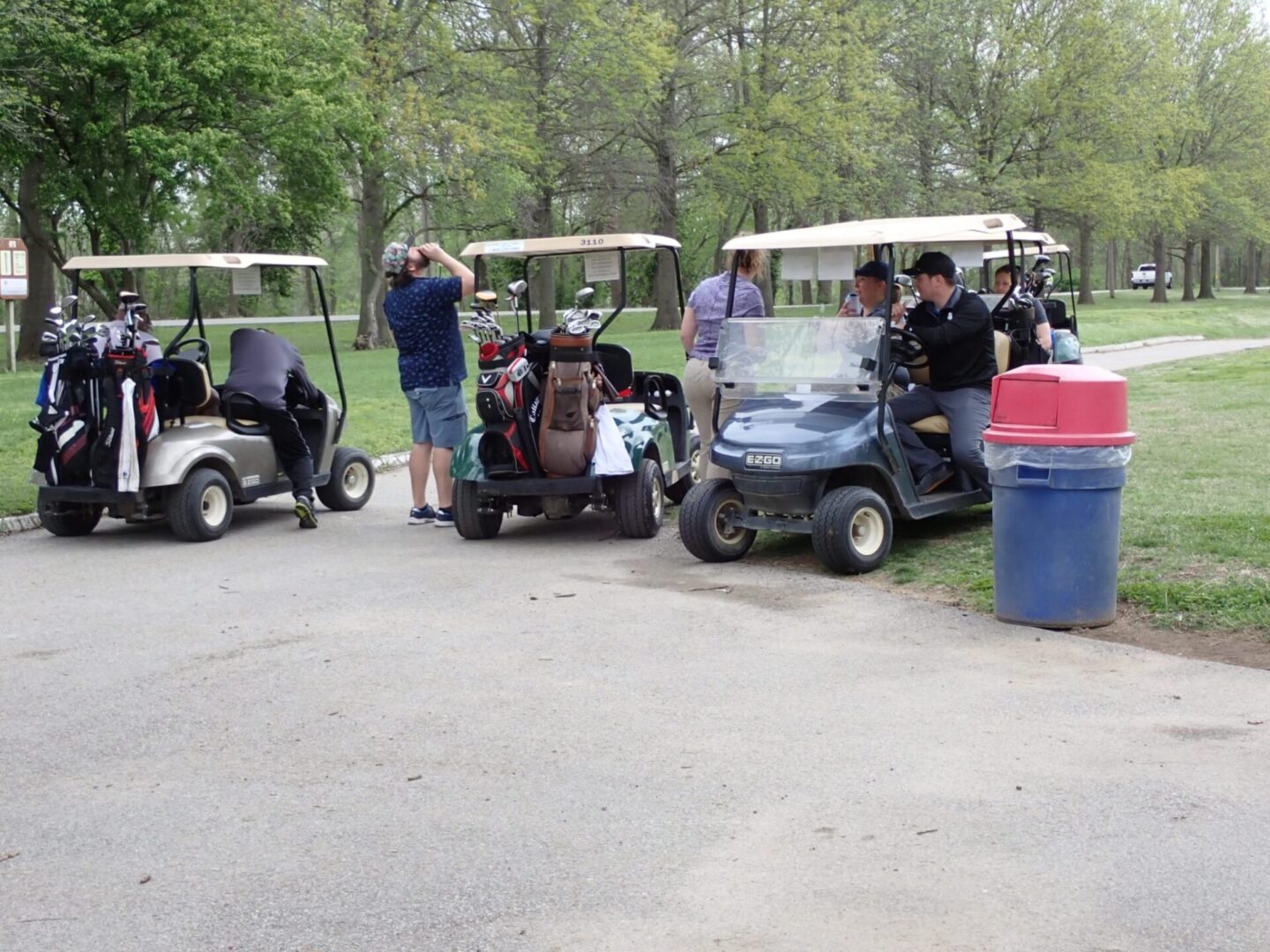People unloading gear from golf carts in a park-like setting.