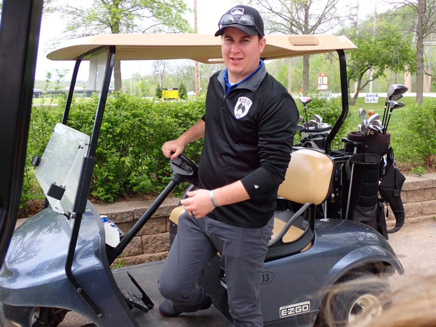 Man kneeling beside a golf cart, smiling and holding the steering wheel.