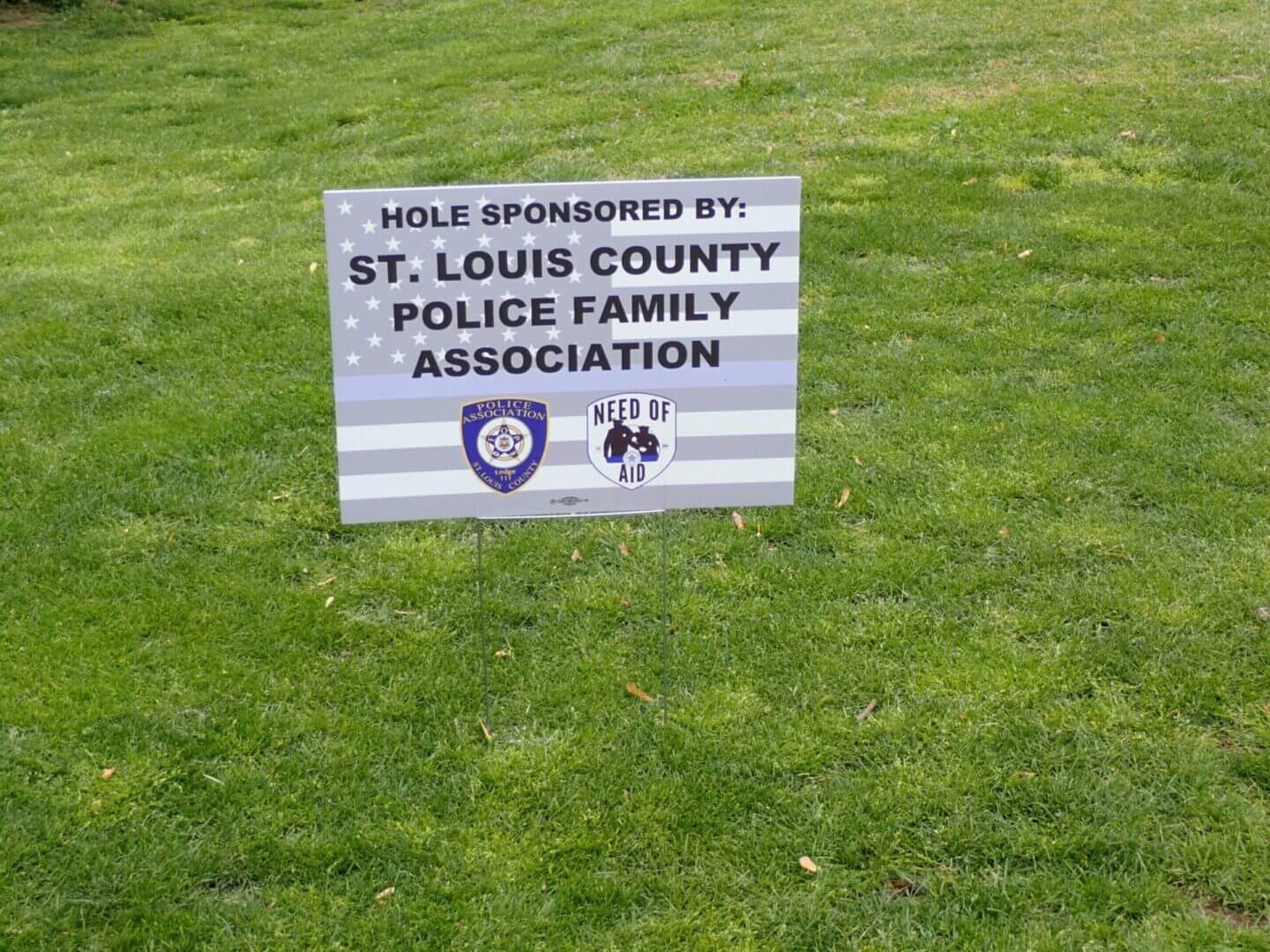 Sign showing hole sponsorship by St. Louis County Police Family Association at a golf course.