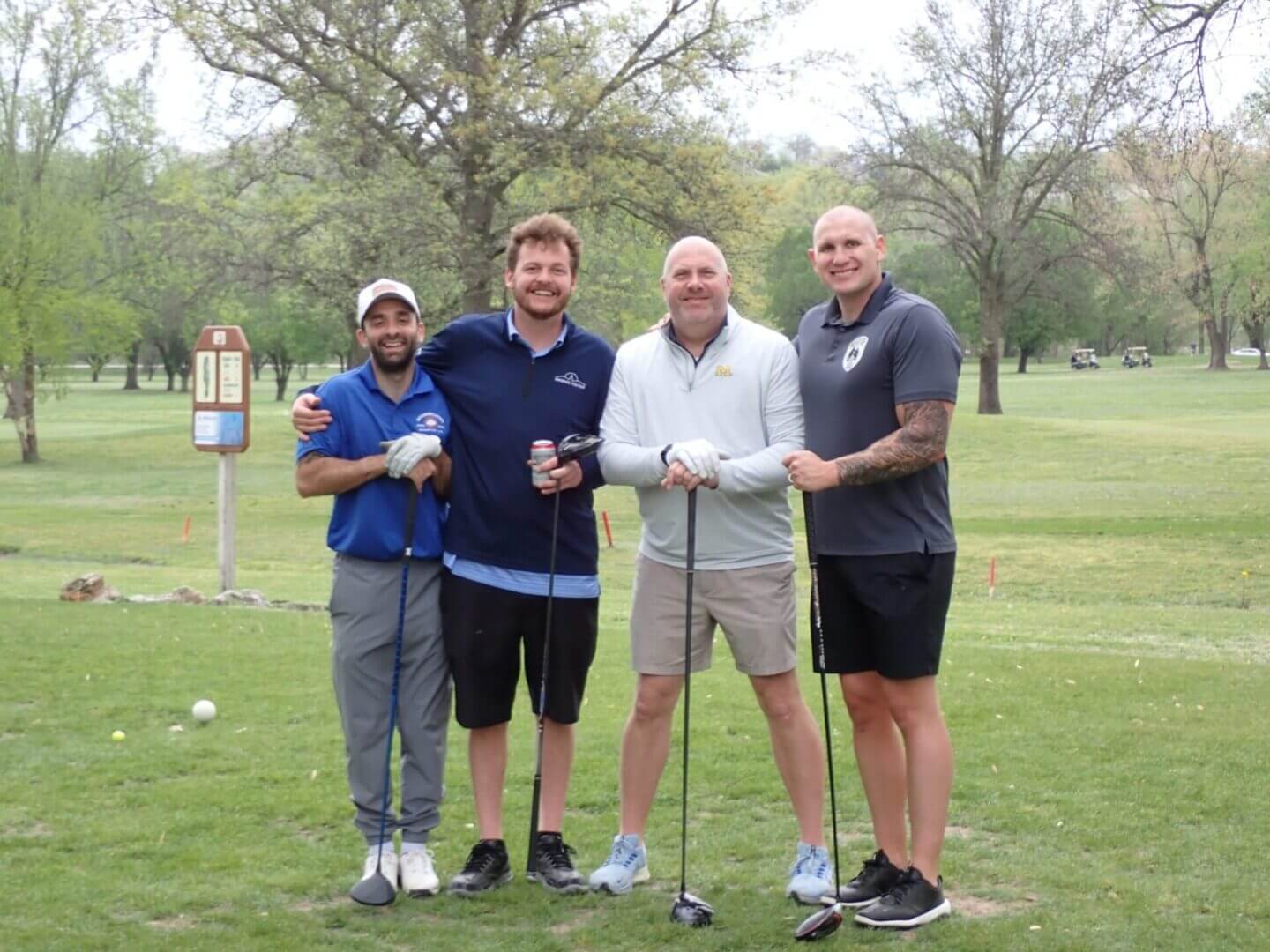 Four men posing together on a golf course with clubs.